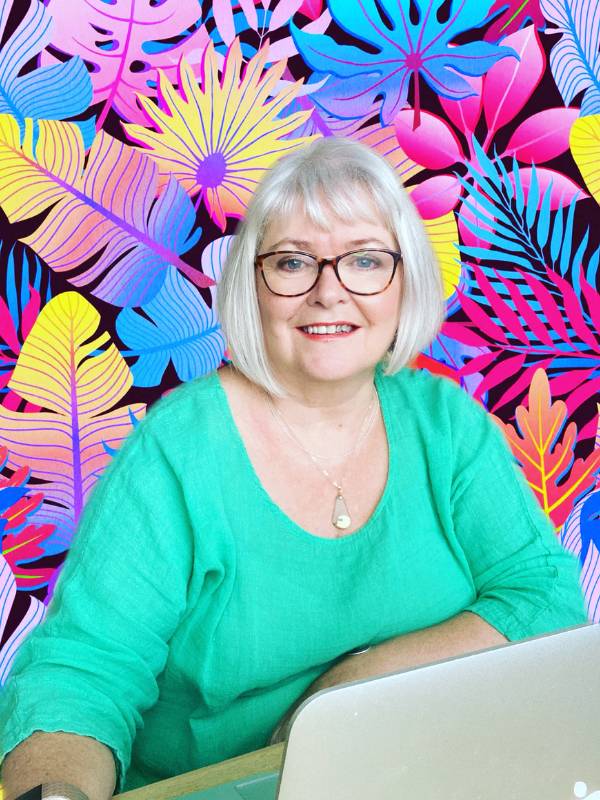 Caucasian white haired woman with glasses and green top sitting at MAC book with jazzy background